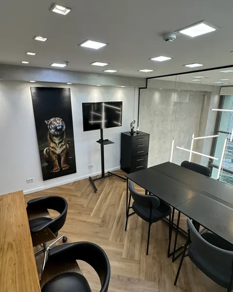 Sala de reunião do estúdio, com mesa preta, cadeiras e quadro de retrato realista na parede.